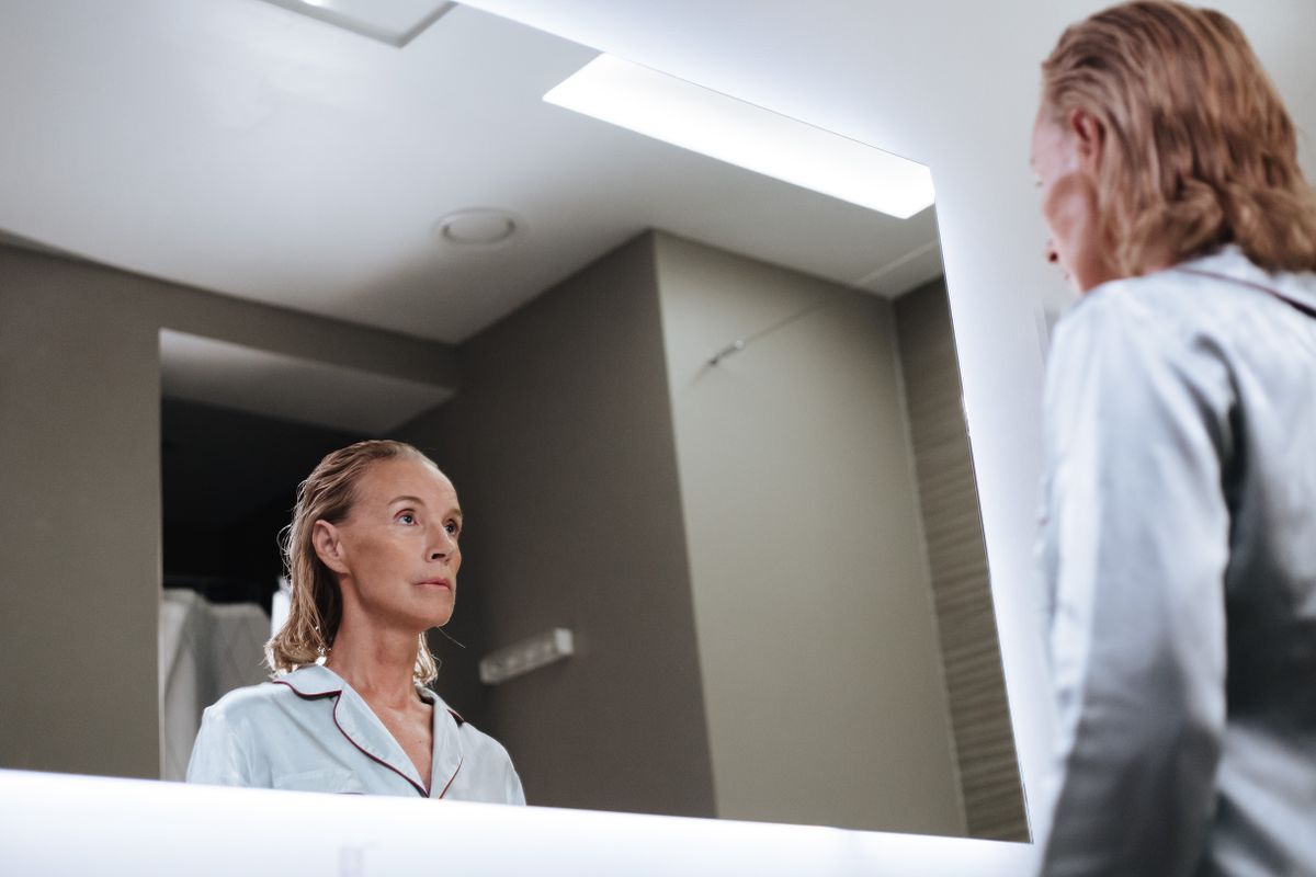 Woman looking at her own reflection in a bathroom mirror, checking how her clothing sits across her body
