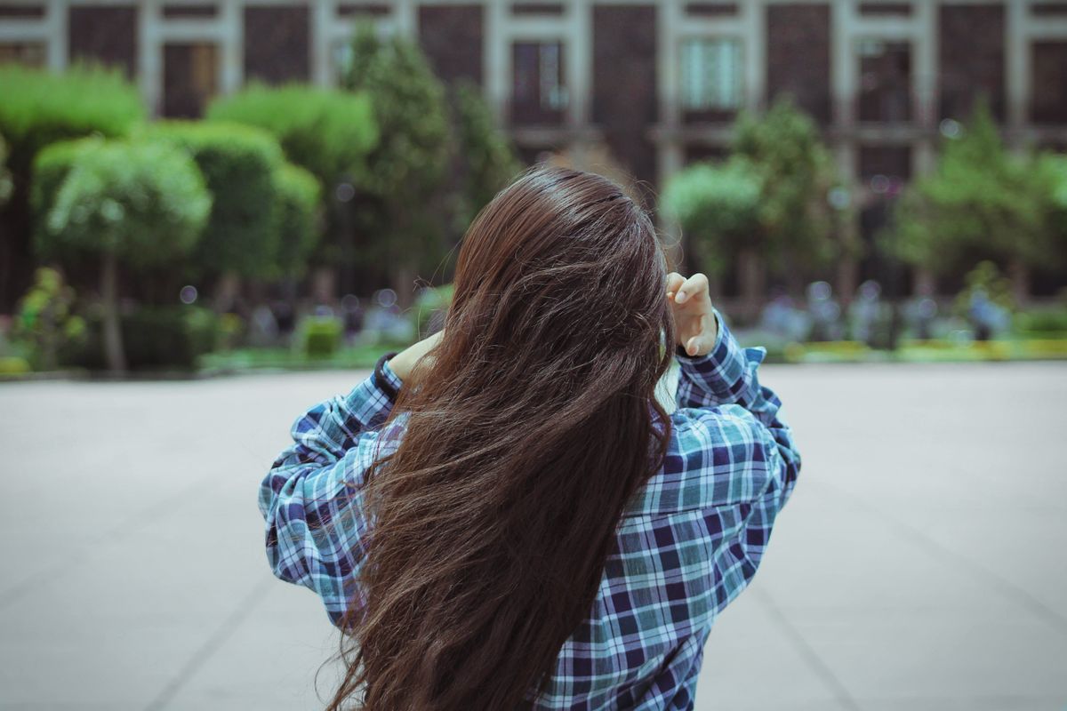 Rear view of a woman in a checked shirt, showing the area across the back where a bra band riding up is easiest to spot