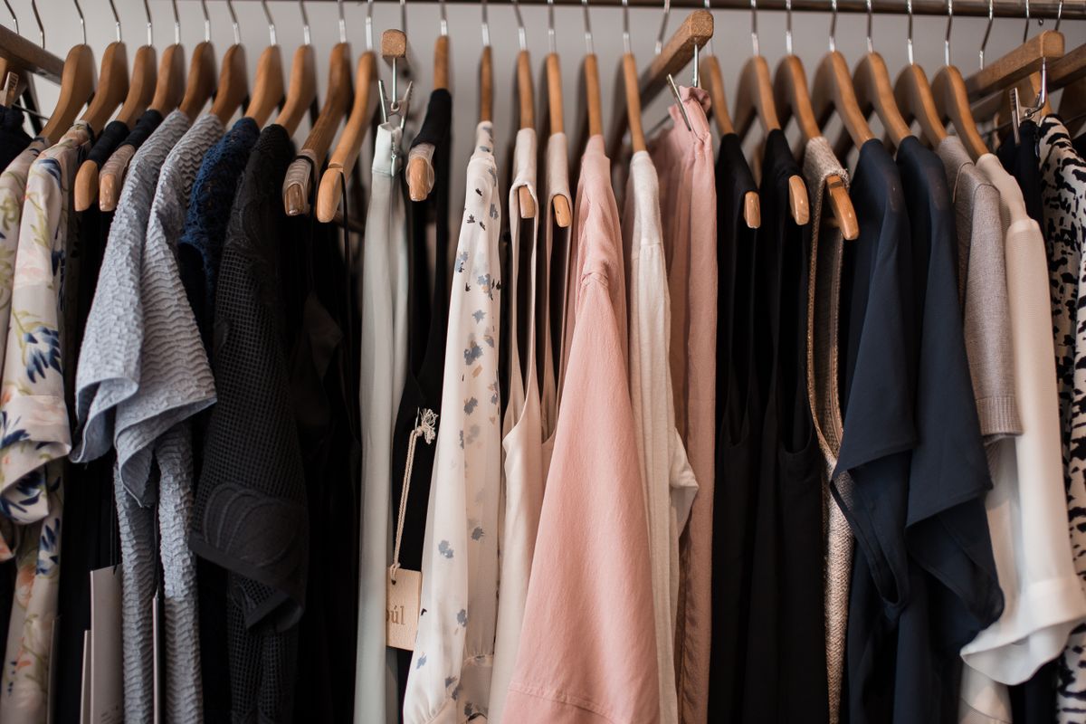 A rail of women's tops and dresses on wooden hangers, showing styles cut higher at the side