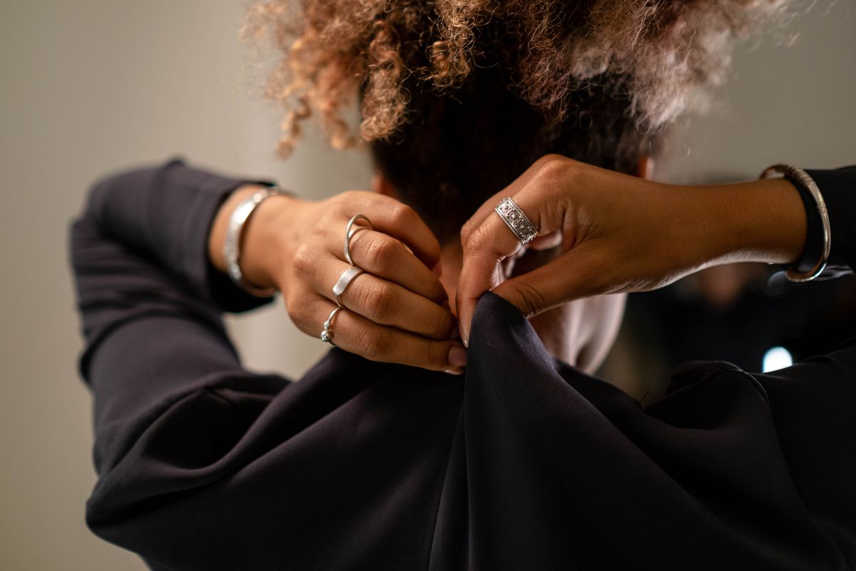 Hands fastening a garment at the back of the neck while getting dressed