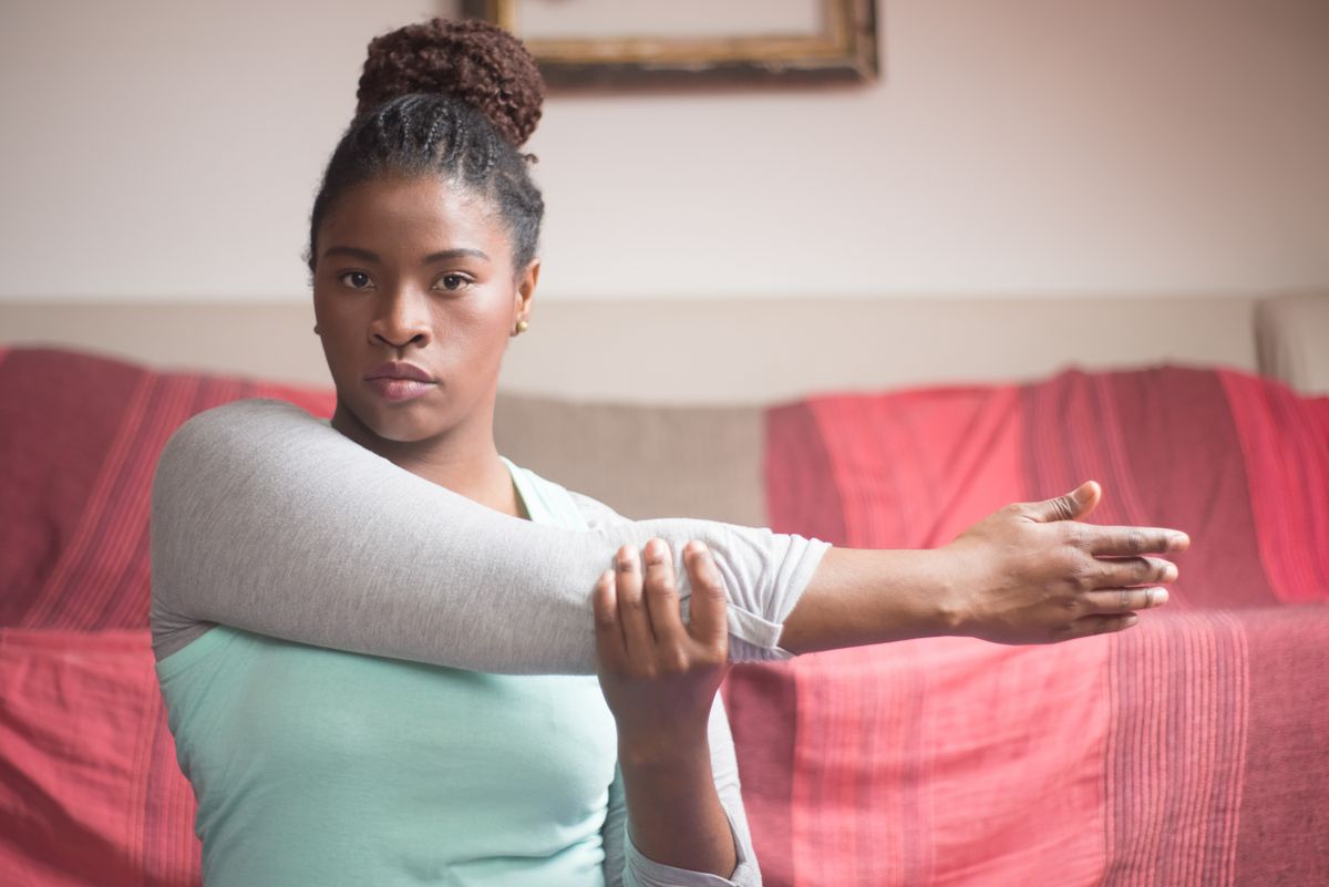 Woman doing an arm and shoulder stretch indoors, the kind of movement that reveals a bra band that will not stay put